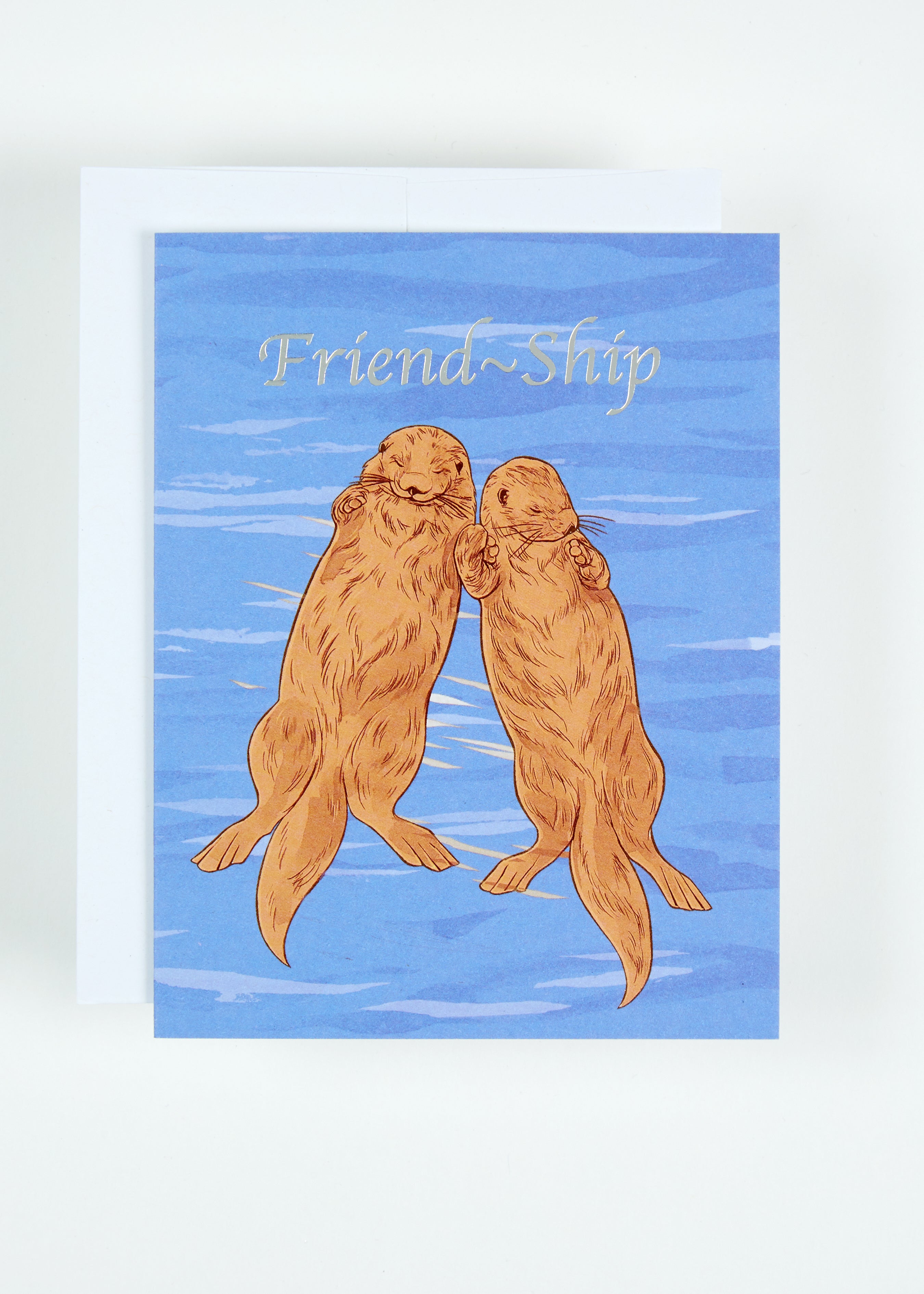 Greeting card printed with the text Friend-Ship and two otters holding hands